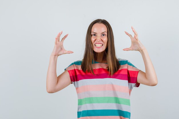 Mujer joven en camiseta levantando las manos de manera agresiva, vista frontal.