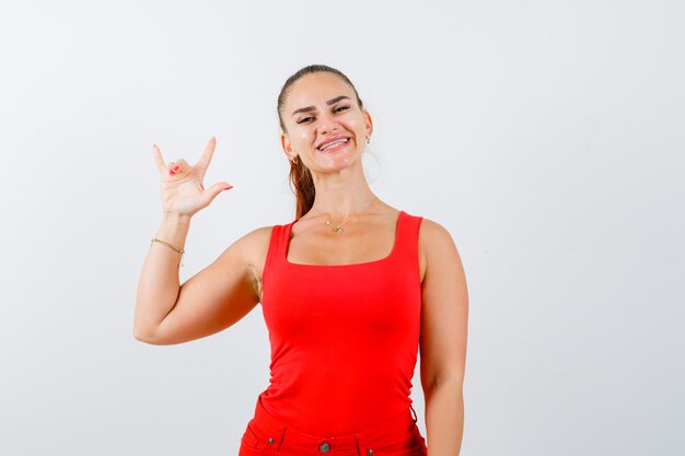 ¿Mujer joven en camiseta sin mangas roja, mostrando los pantalones? Amo tu gesto y luciendo lindo, vista frontal.