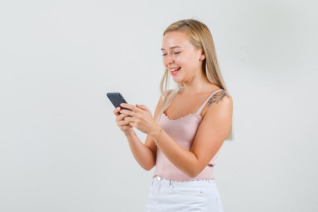 Mujer joven en camiseta, mini falda escribiendo en el teléfono inteligente y sonriendo.