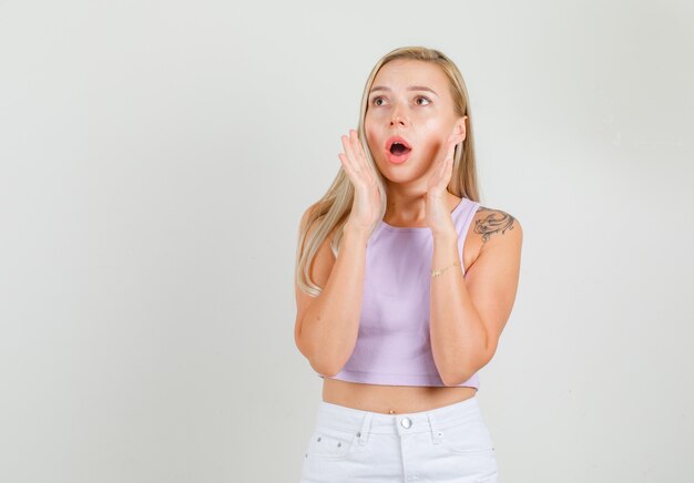 Mujer joven en camiseta, mini falda gritando con las manos cerca de la boca y mirando emocionado