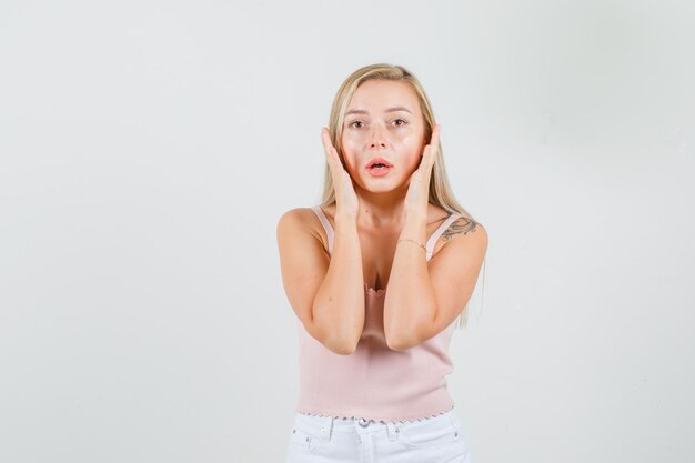 Mujer joven en camiseta, mini falda manteniendo las manos cerca de la cara y luciendo decepcionada