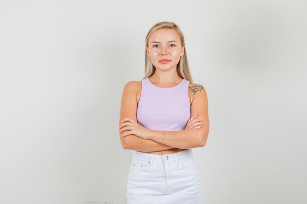 Mujer joven en camiseta, mini falda de pie con los brazos cruzados y mirando confiado