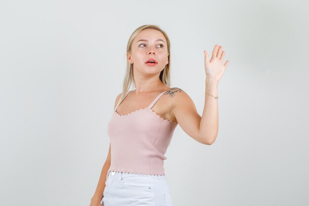 Mujer joven en camiseta, minifalda agitando la mano para decir adiós y mirando confiado