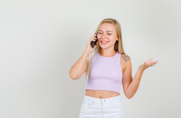 Mujer joven en camiseta, minifalda hablando por teléfono y sonriendo