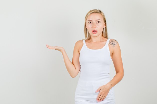 Mujer joven en camiseta, minifalda manteniendo la palma abierta levantada y mirando sorprendido