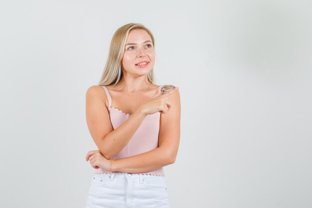 Mujer joven en camiseta, minifalda mirando hacia arriba mientras apunta lejos y parece contento