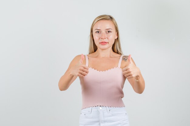 Mujer joven en camiseta, minifalda mostrando los pulgares hacia arriba y mirando confiado