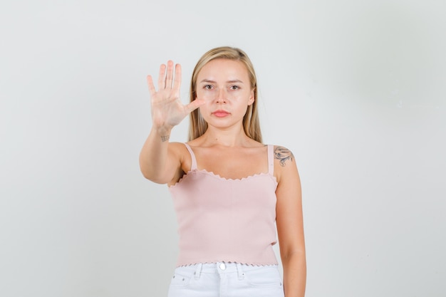 Mujer joven en camiseta, minifalda mostrando la señal de pare con la mano y mirando seria