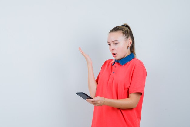 Mujer joven en camiseta mirando el teléfono móvil y mirando ansioso