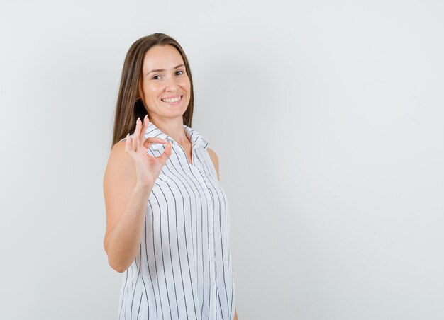 Mujer joven en camiseta mostrando gesto ok y mirando alegre, vista frontal.