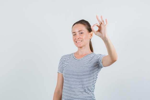 Mujer joven en camiseta mostrando gesto ok y mirando alegre, vista frontal.