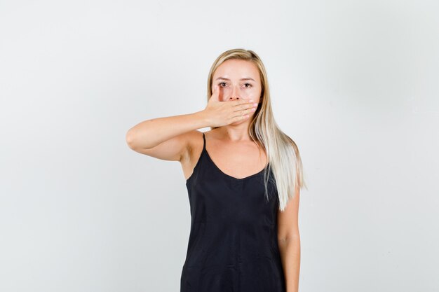 Mujer joven en camiseta negra cubriendo la boca con la mano y mirando seria