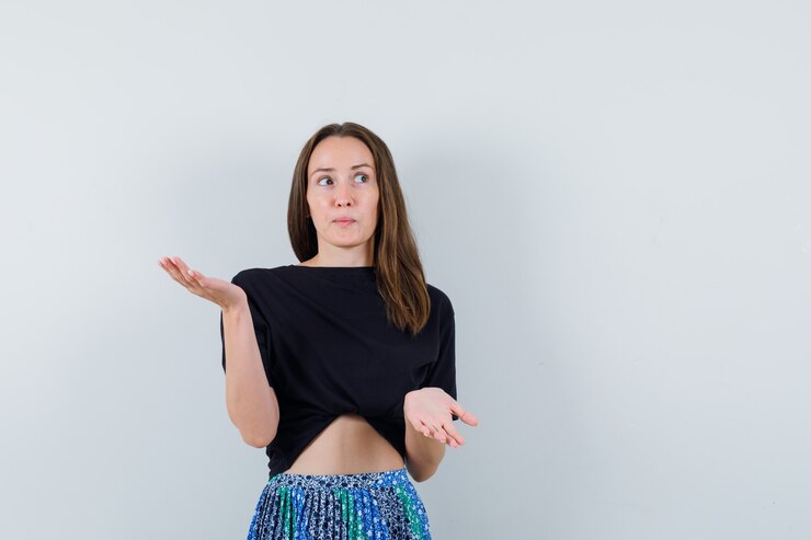 Foto gratuito mujer joven en camiseta negra y falda azul levantando una mano mientras sostiene algo mientras estira la otra mano para recibir algo y lucir atractivo