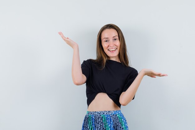 Mujer joven en camiseta negra y falda azul que muestra un gesto de impotencia y parece feliz