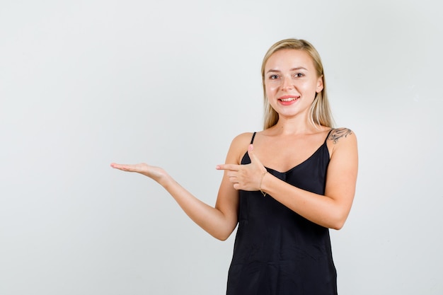 Mujer joven en camiseta negra mostrando o presentando algo y luciendo alegre