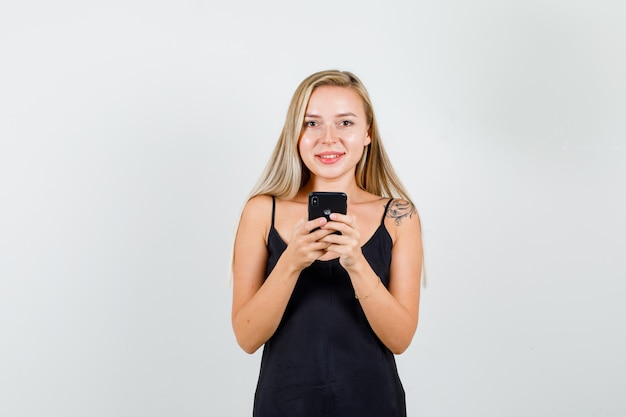 Mujer joven en camiseta negra con smartphone y mirando alegre