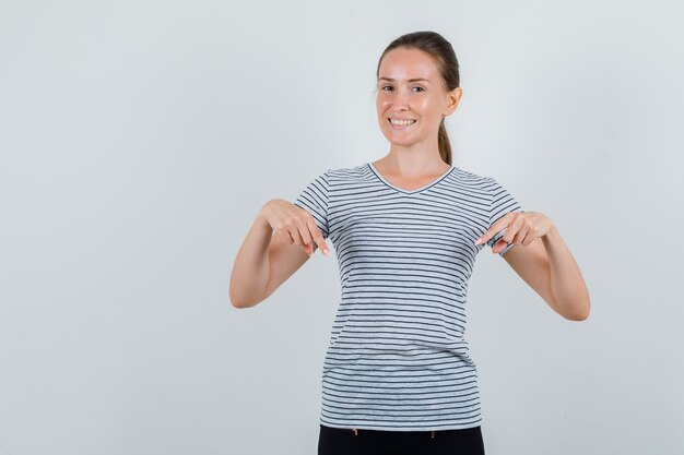 Mujer joven en camiseta, pantalones apuntando hacia abajo y mirando alegre, vista frontal.