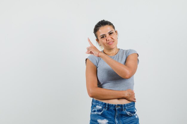 Mujer joven en camiseta, pantalones cortos apuntando hacia arriba y mirando confiado