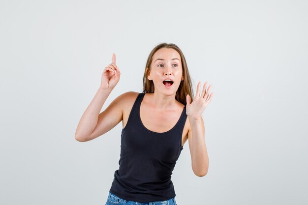 Mujer joven en camiseta, pantalones cortos apuntando con el dedo hacia arriba con signo de mano