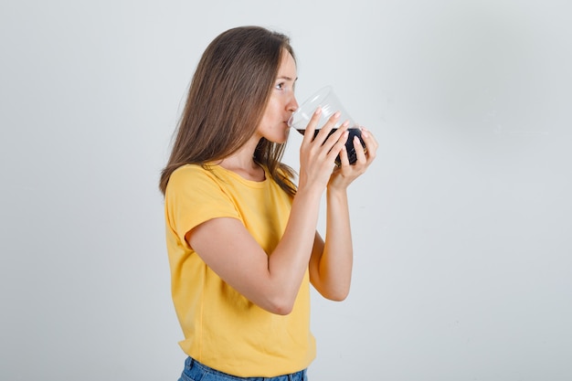 Mujer joven en camiseta, pantalones cortos bebiendo refresco de cola y mirando sediento.