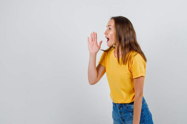 Mujer joven en camiseta, pantalones cortos gritando a alguien con signo de mano.