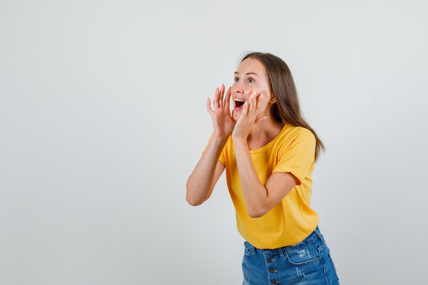 Mujer joven en camiseta, pantalones cortos gritando o anunciando algo y mirando contento