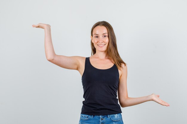 Mujer joven en camiseta, pantalones cortos manteniendo las palmas abiertas y mirando alegre