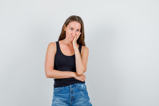 Mujer joven en camiseta, pantalones cortos mirando a otro lado con la mano en la mejilla y mirando lo siento