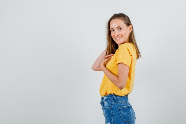 Mujer joven en camiseta, pantalones cortos, posando mientras toca el cabello y luciendo encantador.