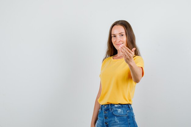 Mujer joven en camiseta, pantalones cortos sonriendo e invitando a venir