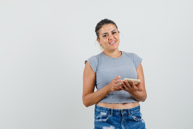 Mujer joven en camiseta, pantalones cortos sosteniendo cuaderno y mirando bastante