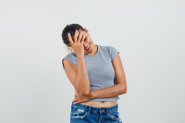 Foto gratuita mujer joven en camiseta, pantalones cortos sosteniendo la mano en la frente y mirando feliz