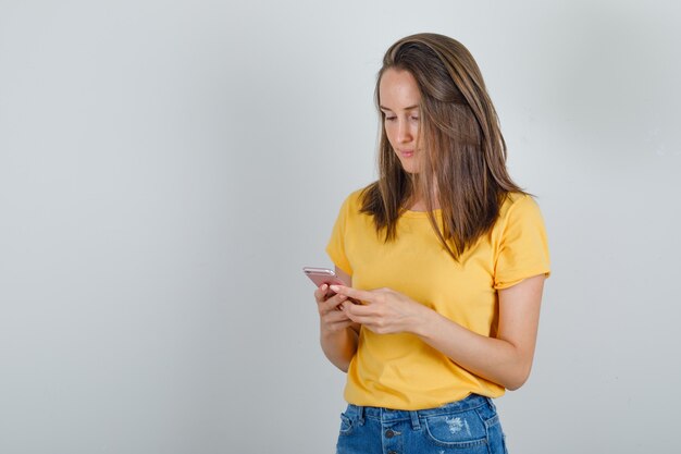 Mujer joven en camiseta, pantalones cortos con teléfono móvil y mirando ocupado