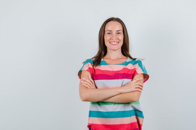 Foto gratuita mujer joven en camiseta de pie con los brazos cruzados y mirando feliz, vista frontal.