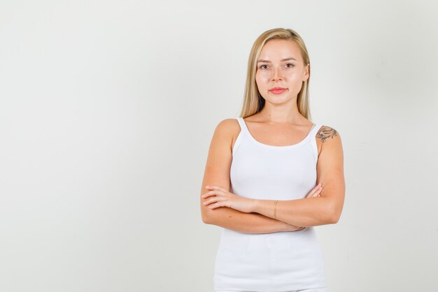 Mujer joven en camiseta de pie con los brazos cruzados y sonriendo