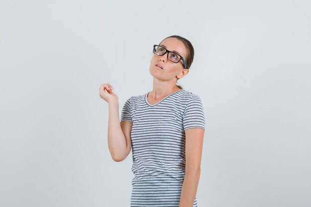 Mujer joven en camiseta a rayas, gafas mirando hacia arriba y mirando pensativo, vista frontal.