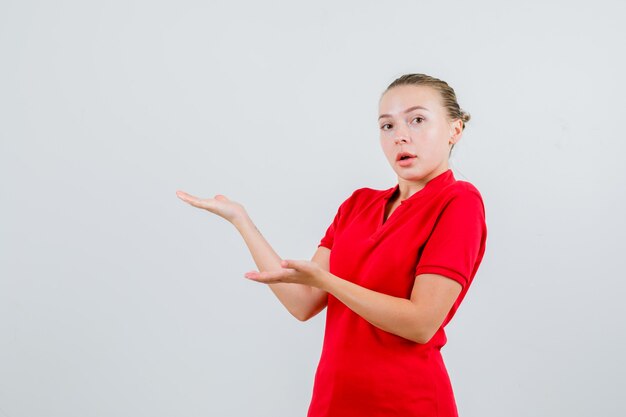 Mujer joven en camiseta roja dando la bienvenida o mostrando algo