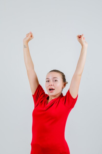 Mujer joven en camiseta roja mostrando gesto de ganador y mirando feliz