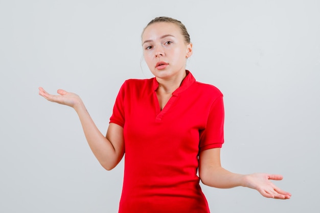 Mujer joven en camiseta roja mostrando gesto de impotencia y mirando desconcertado