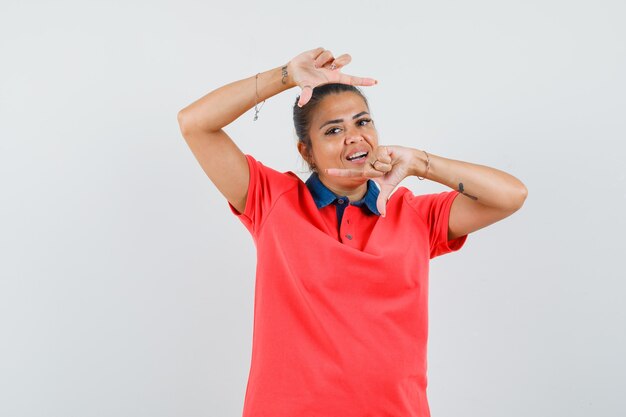 Mujer joven en camiseta roja mostrando el pulgar hacia abajo y estirando una mano y luciendo bonita vista frontal.