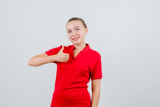 Mujer joven en camiseta roja mostrando el pulgar hacia arriba y mirando feliz