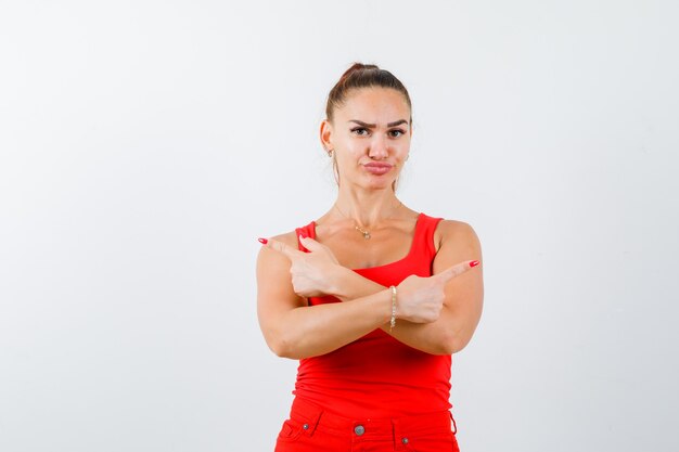 Mujer joven en camiseta roja, pantalones apuntando a ambos lados y mirando vacilante, vista frontal.