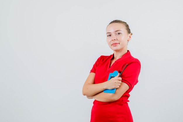 Mujer joven en camiseta roja sosteniendo mini portapapeles y mirando optimista