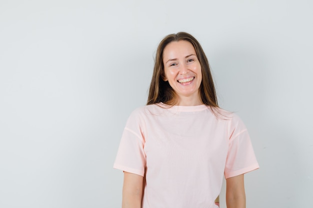 Mujer joven en camiseta rosa y mirando alegre, vista frontal.