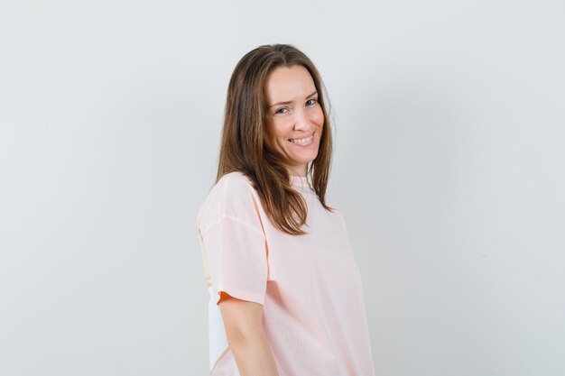 Mujer joven en camiseta rosa y mirando alegre, vista frontal.