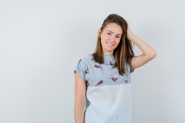 Mujer joven en camiseta sosteniendo la mano sobre el cabello y mirando seductor, vista frontal.