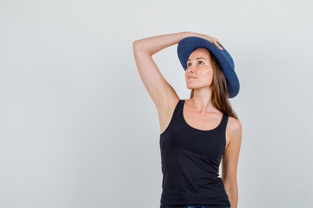 Mujer joven en camiseta, sosteniendo la mano en el sombrero mientras posa