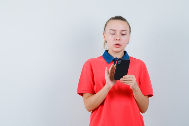 Mujer joven en camiseta con teléfono móvil y mirando ocupado