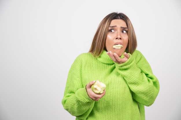 Mujer joven en camiseta verde comiendo una manzana.