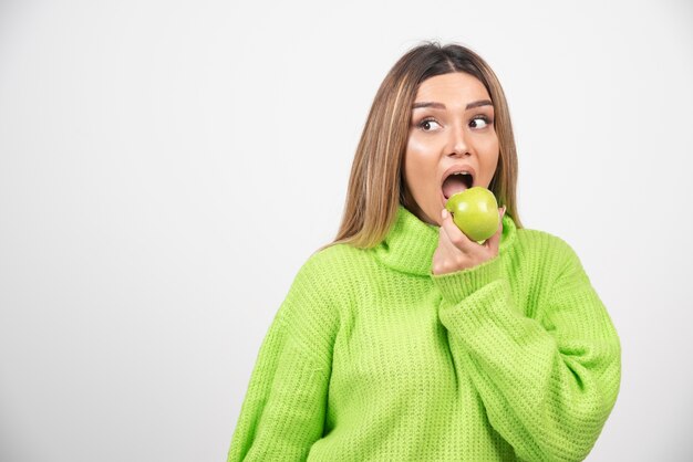 Mujer joven en camiseta verde comiendo una manzana